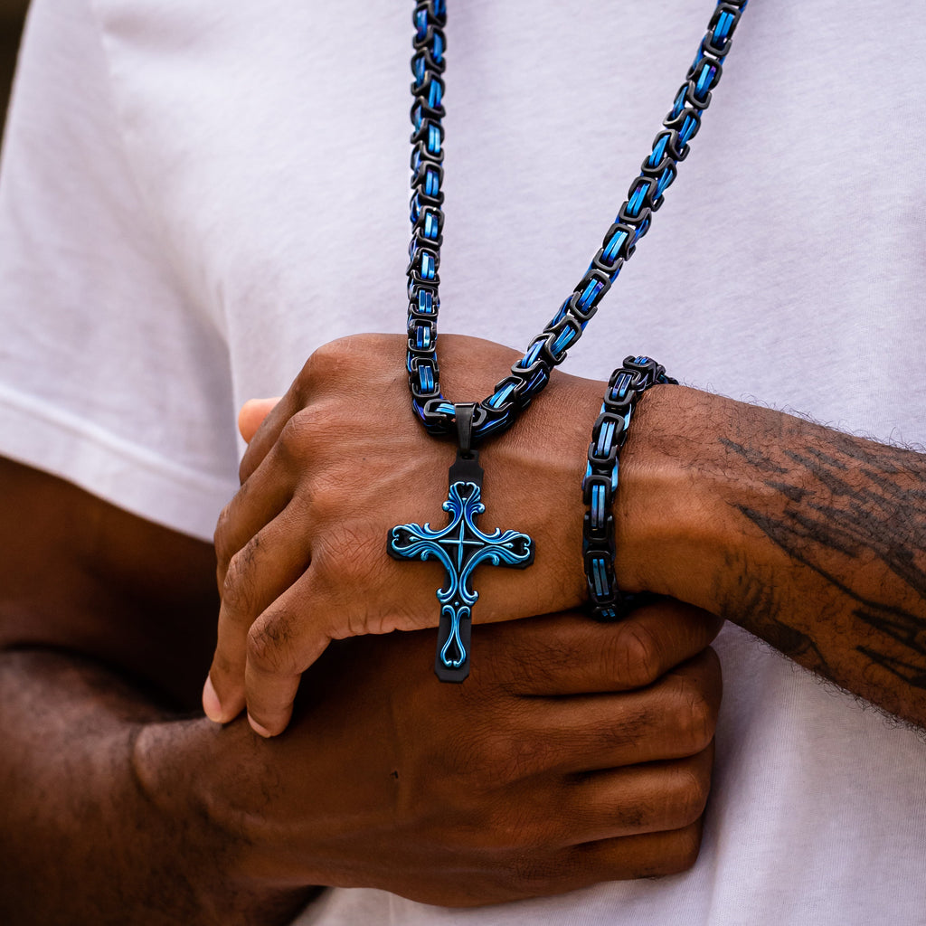 Person wearing a blue chain necklace with a cross pendant, holding hands together.